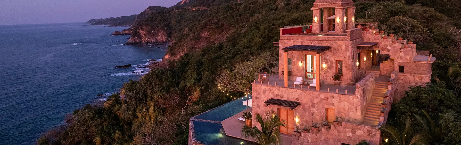 Luxury cliffside villas surrounded by lush jungle, overlooking the ocean at dusk.